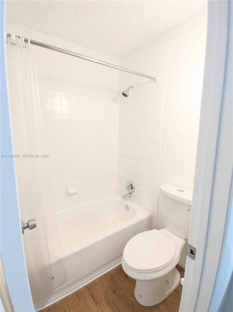 4401 W Mcnab Road, Pompano Beach, FL 33069 Bathroom featuring a porcelain tub, wall-mounted shower head, white ceramic tile surround, and wood-finish flooring