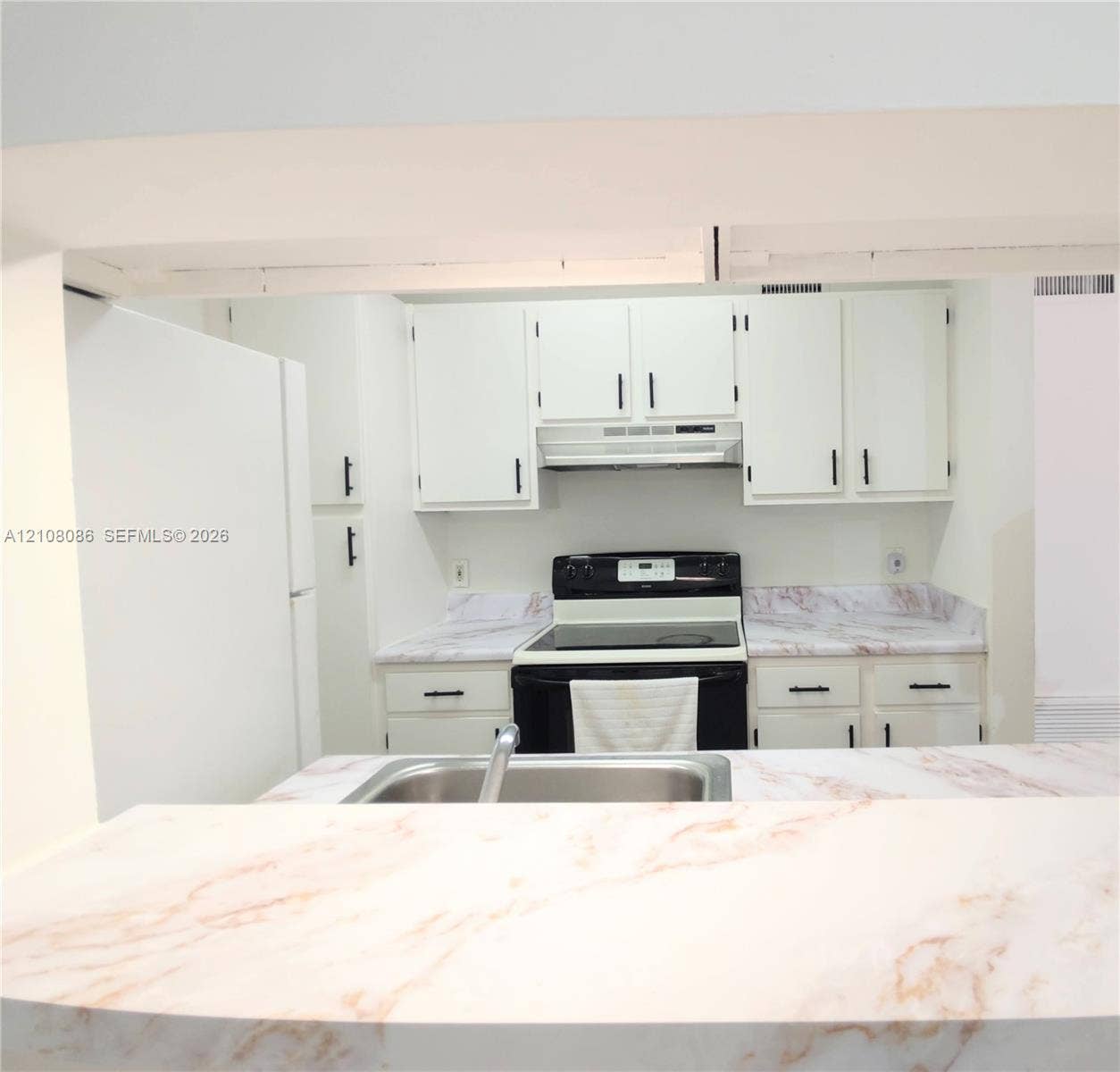 4401 W Mcnab Road, Pompano Beach, FL 33069 Kitchen featuring white cabinetry with dark hardware, stone-patterned countertops, a stainless steel sink, and a built-in range hood