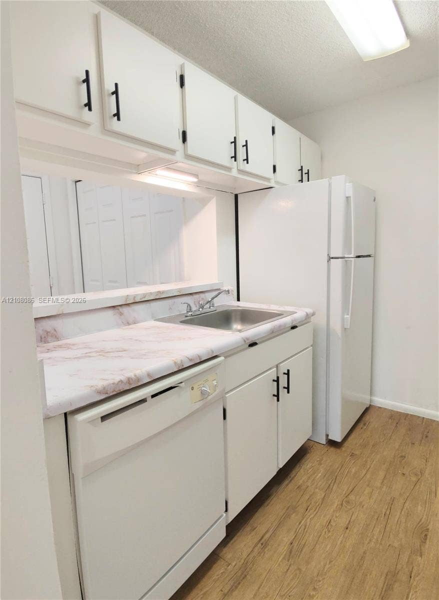 4401 W Mcnab Road, Pompano Beach, FL 33069 Kitchen featuring white cabinetry with matte black hardware, stone-pattern laminate countertops, stainless steel sink with a dual-handle faucet, and wood-finish flooring