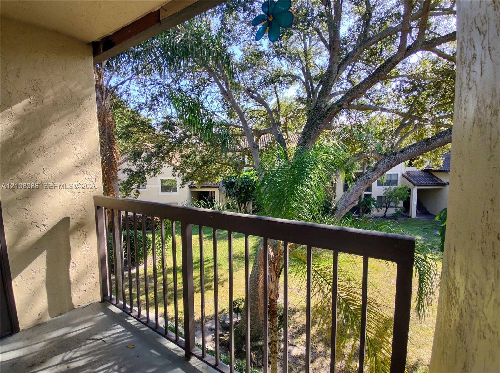 4401 W Mcnab Road, Pompano Beach, FL 33069 Covered balcony with metal railing, stucco walls, and mature landscaping