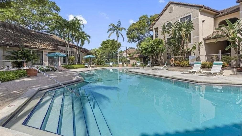 4401 W Mcnab Road, Pompano Beach, FL 33069 Community swimming pool featuring a concrete deck, built-in entry steps with handrails, and surrounding tropical landscaping