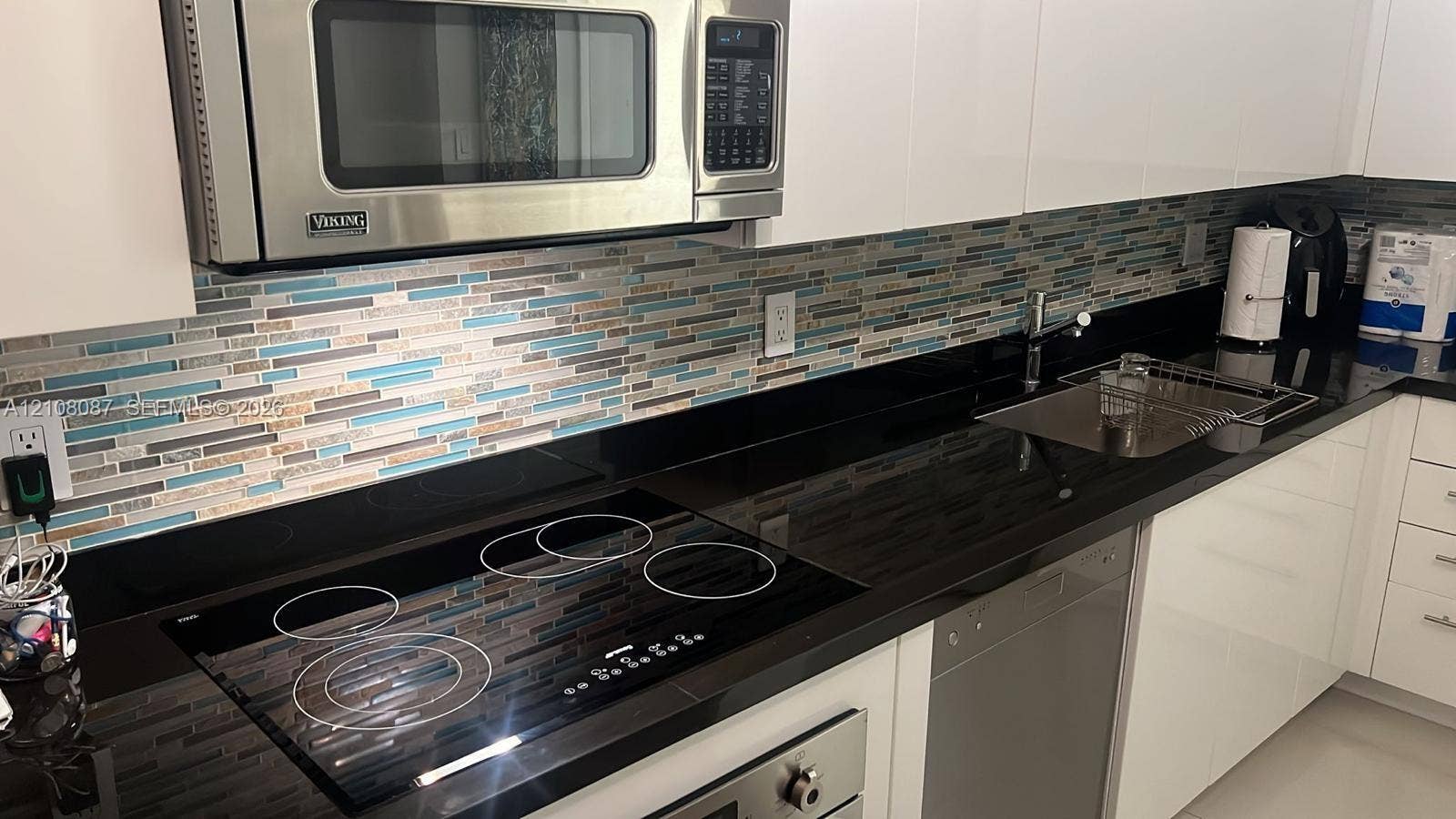 92 SW 3rd Street, #5008, Miami, Miami, FL 33130 Kitchen featuring white flat-panel cabinetry, dark solid-surface countertops, stainless steel microwave, glass-top electric range, and mosaic tile backsplash