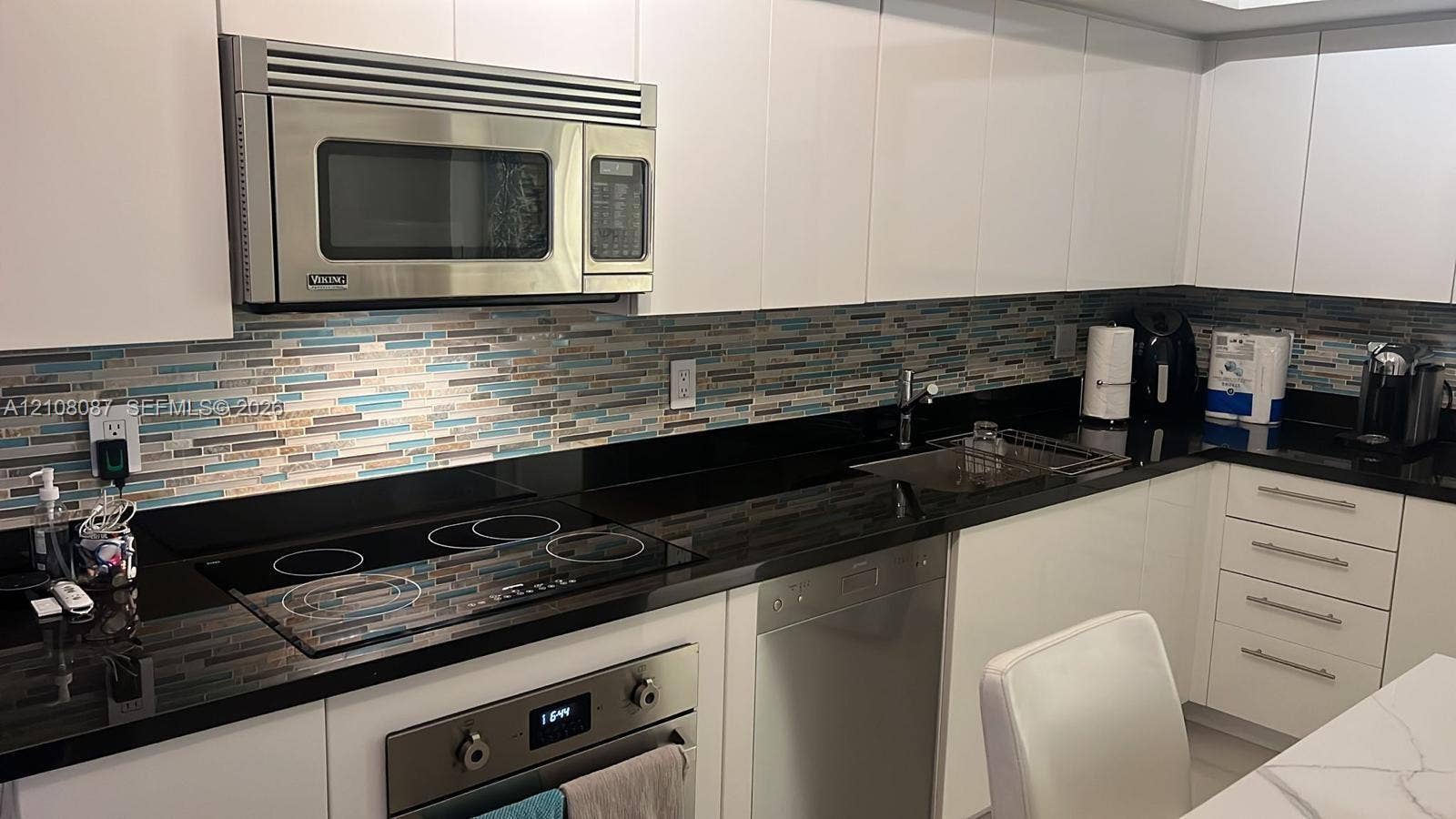 92 SW 3rd Street, #5008, Miami, Miami, FL 33130 Kitchen featuring white slab cabinetry, black countertops, multi-toned glass tile backsplash, stainless steel built-in microwave, and electric cooktop
