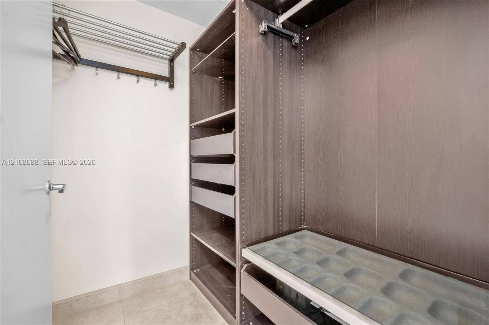 333 Las Olas Way, #2601, Fort Lauderdale, FL 33301 Walk-in closet featuring custom wood-finish cabinetry, built-in shelving, integrated pull-out drawers, a glass-topped accessory organizer, and wall-mounted garment racks