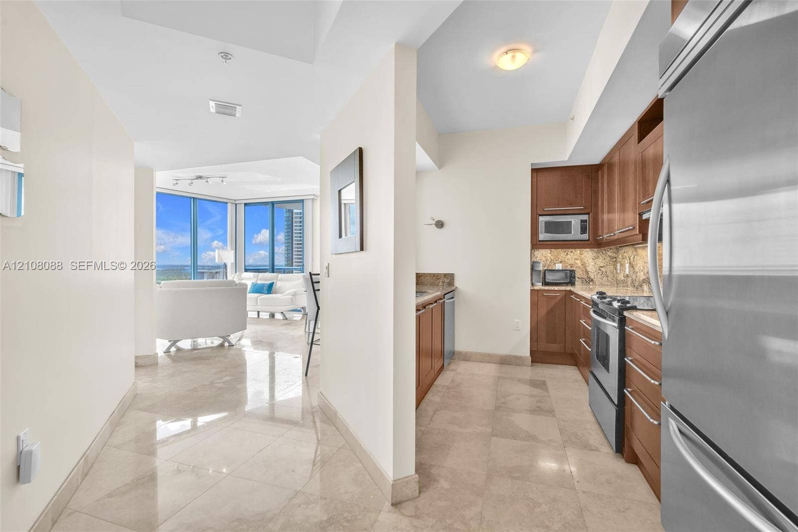333 Las Olas Way, #2601, Fort Lauderdale, FL 33301 Entry and kitchen featuring wood cabinetry, stone countertops, stone flooring, and stainless steel appliances, with floor-to-ceiling windows