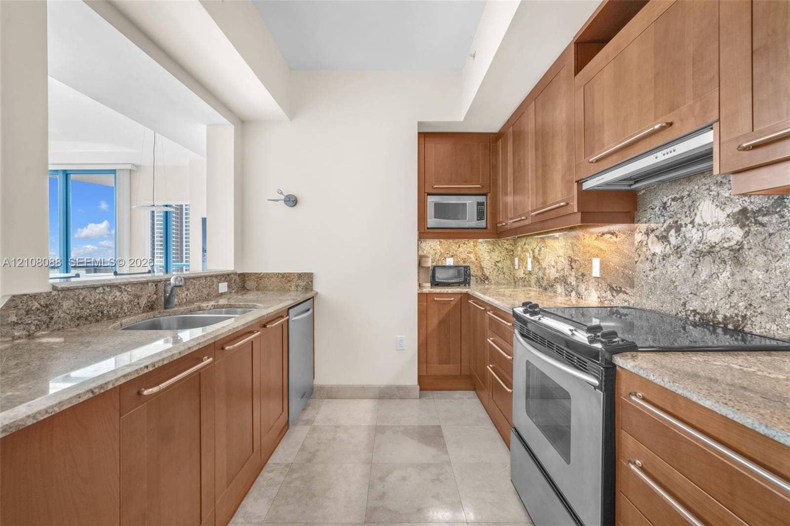 333 Las Olas Way, #2601, Fort Lauderdale, FL 33301 Kitchen featuring wood cabinetry, stone countertops, stone backsplash, stainless steel appliances, and large-format tile flooring