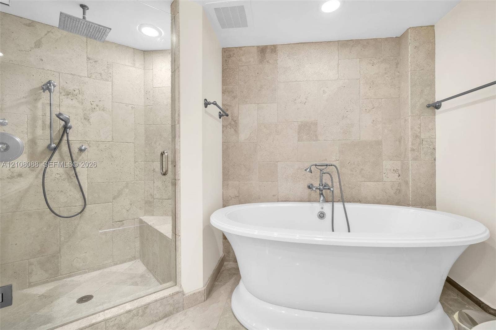333 Las Olas Way, #2601, Fort Lauderdale, FL 33301 Freestanding soaking tub with chrome telephone-style faucet, glass-enclosed walk-in shower featuring a built-in bench, ceiling-mounted rainfall showerhead, and stone tile surround