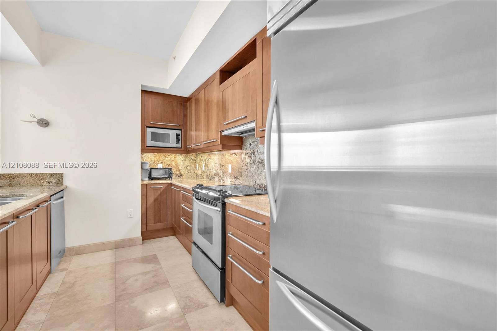 333 Las Olas Way, #2601, Fort Lauderdale, FL 33301 Kitchen featuring natural wood cabinetry, stone countertops, stone tile backsplash, stainless steel appliances, and large-format tile flooring