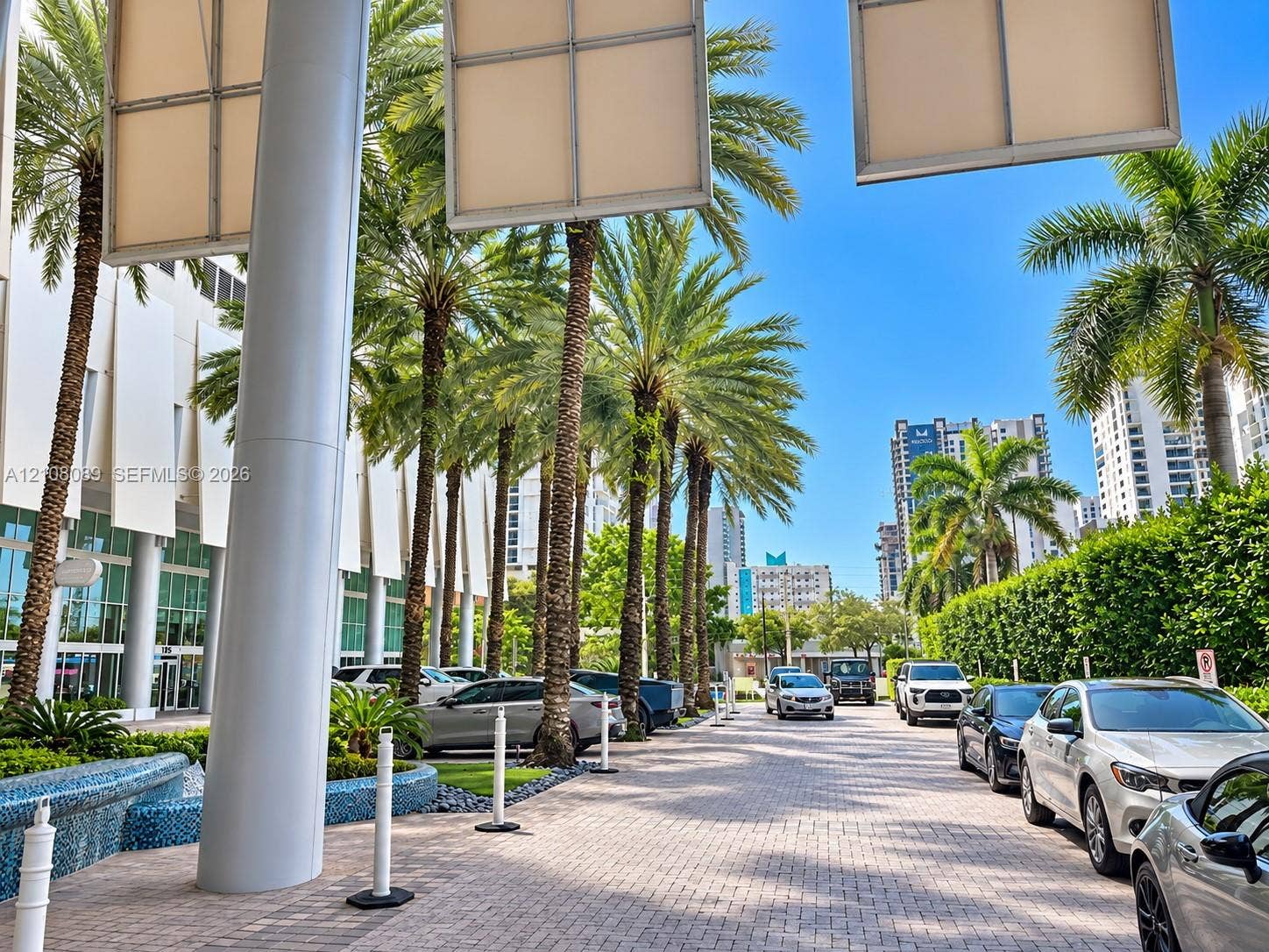 185 SW 7th Street, #3608, Miami, FL 33130 Paver-stone drive featuring towering palm trees, a blue mosaic tile water feature, structural columns, and large-scale architectural wall panels