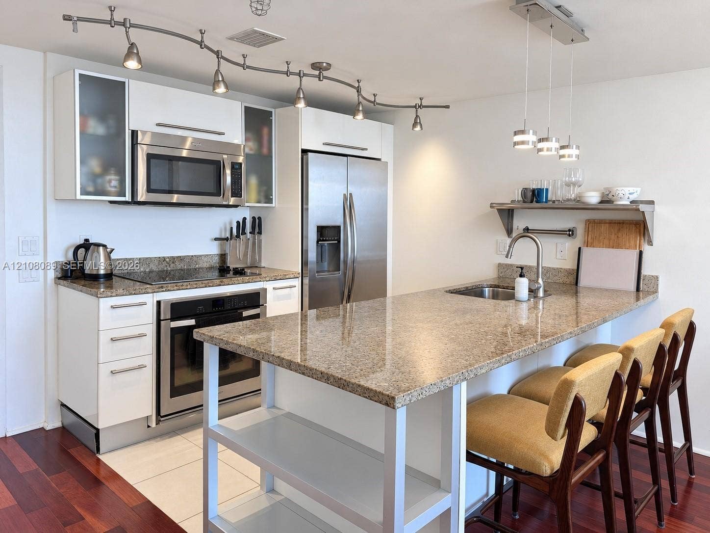 185 SW 7th Street, #3608, Miami, FL 33130 Kitchen featuring stone countertops, stainless steel appliances, white cabinetry with glass-front uppers, an integrated island with shelving, and track lighting