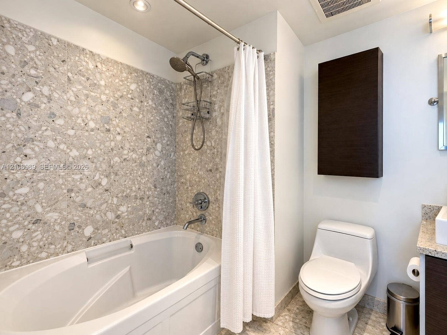 185 SW 7th Street, #3608, Miami, FL 33130 Bathroom featuring a soaking tub with stone-tiled surround, handheld shower fixture, dual-flush toilet, wall-mounted storage cabinet, and vanity with stone countertop