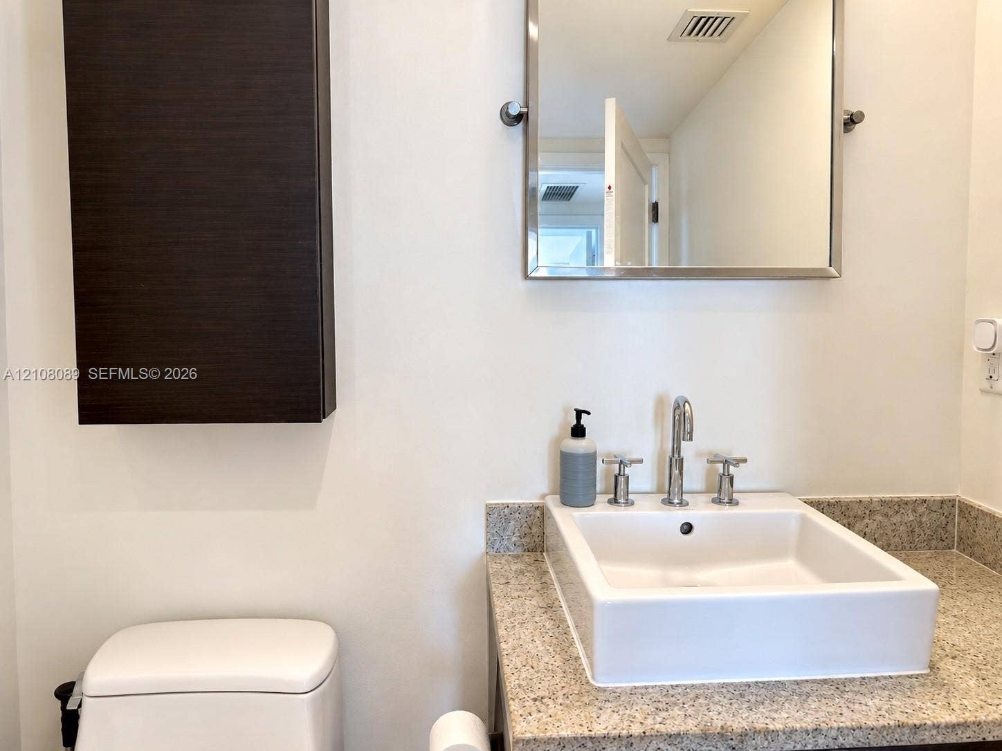185 SW 7th Street, #3608, Miami, FL 33130 Bathroom vanity featuring a vessel sink, stone-finish countertop, wall-mounted dark wood-finish cabinetry, and a chrome-framed mirror with chrome widespread faucet