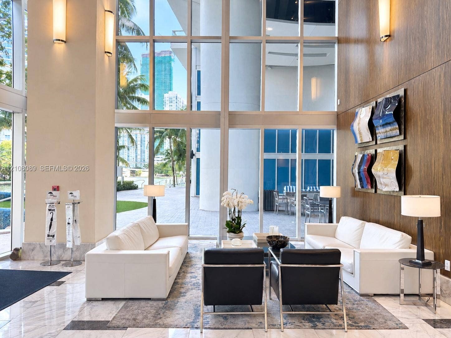 185 SW 7th Street, #3608, Miami, FL 33130 Double-height floor-to-ceiling windows, polished stone flooring, wood-paneled feature wall, and wall-mounted metal light fixtures