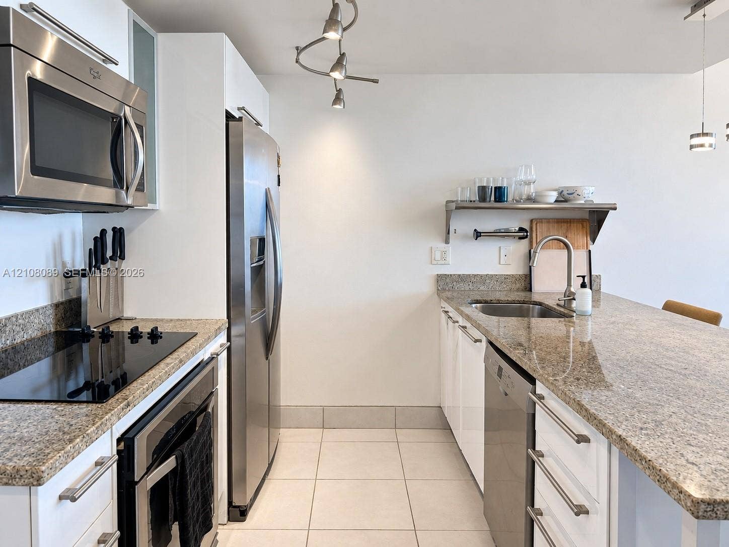 185 SW 7th Street, #3608, Miami, FL 33130 Kitchen featuring stone countertops, stainless steel appliances, white cabinetry, a built-in wall-mounted shelf, and tile flooring