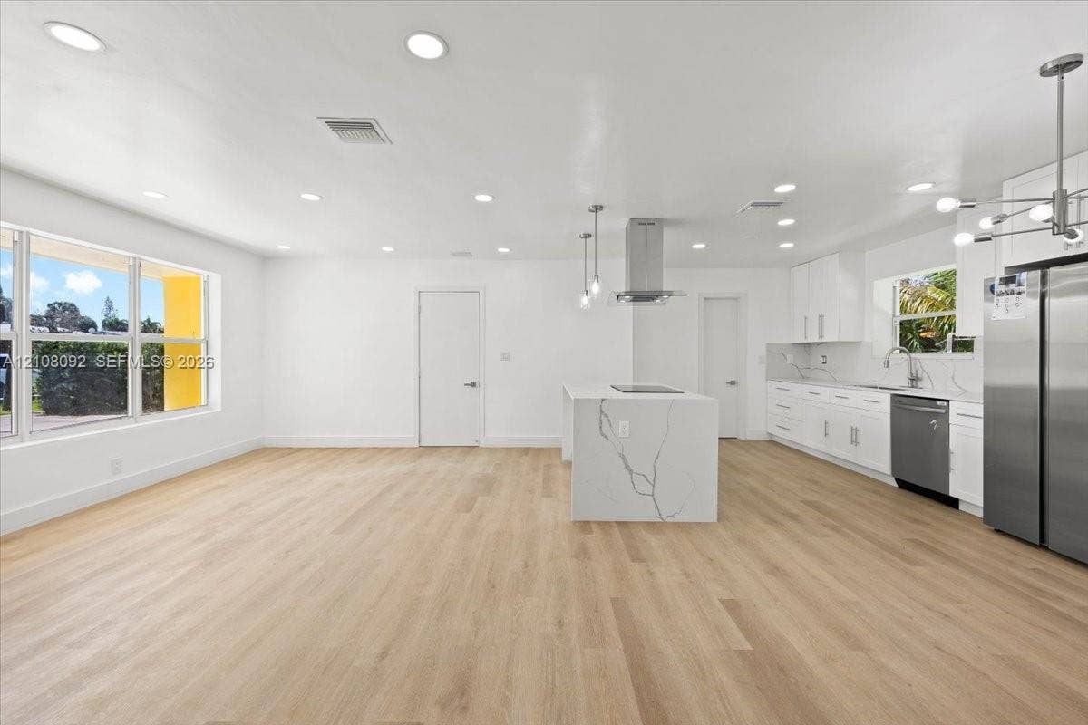Hallway featuring wood-finish flooring, crisp white walls, recessed ceiling lighting, and louvered closet doors