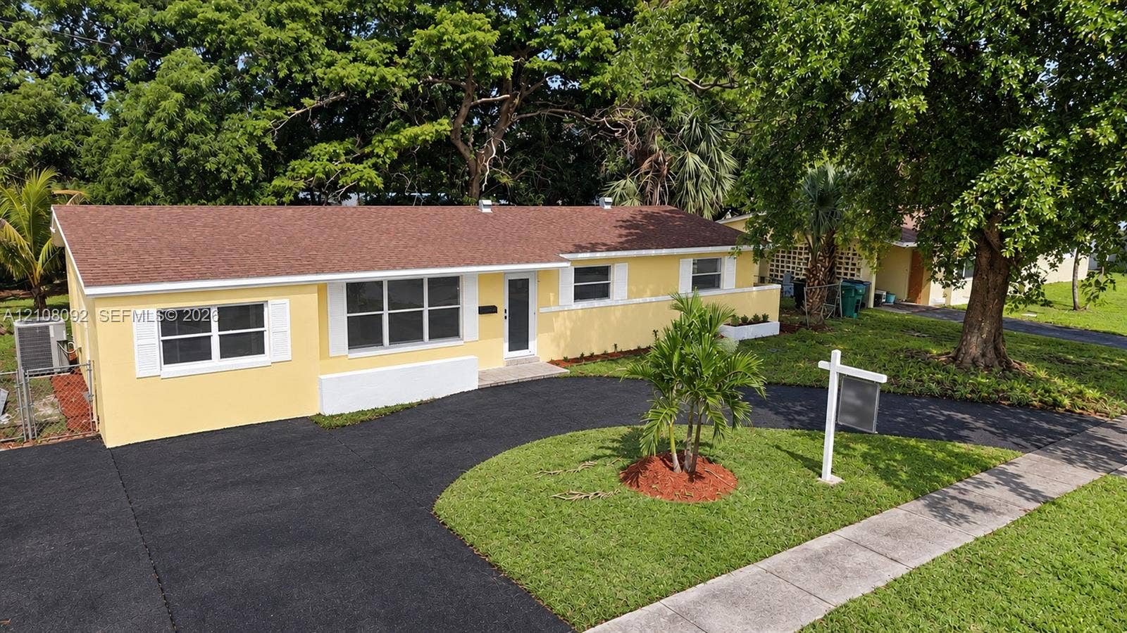 Single-story residence featuring a paved curved driveway, multi-pane windows with white exterior shutters, and mature trees
