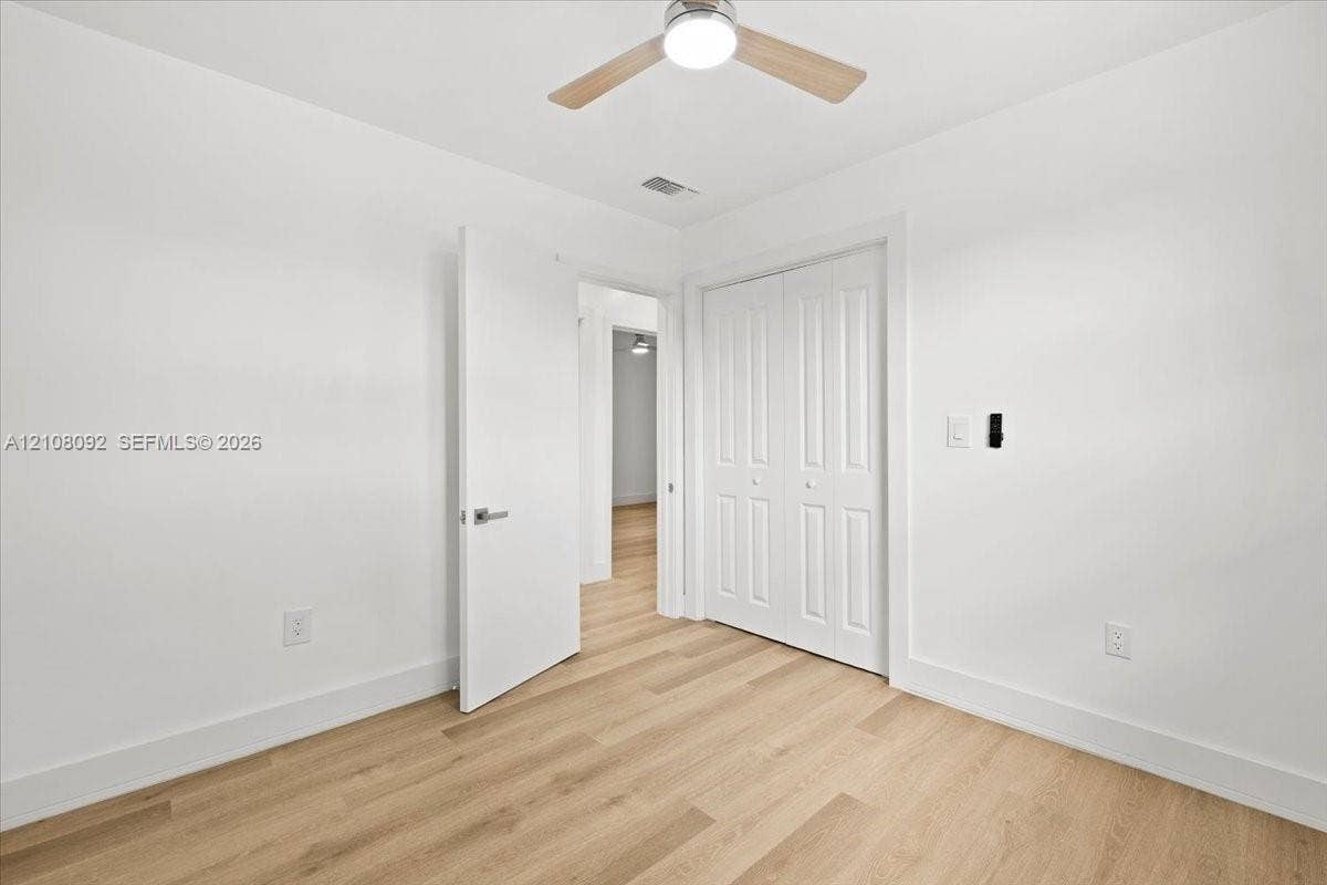 Neutral-toned room featuring wood-finish flooring, a ceiling fan with integrated lighting, a single-pane window, and white interior doors