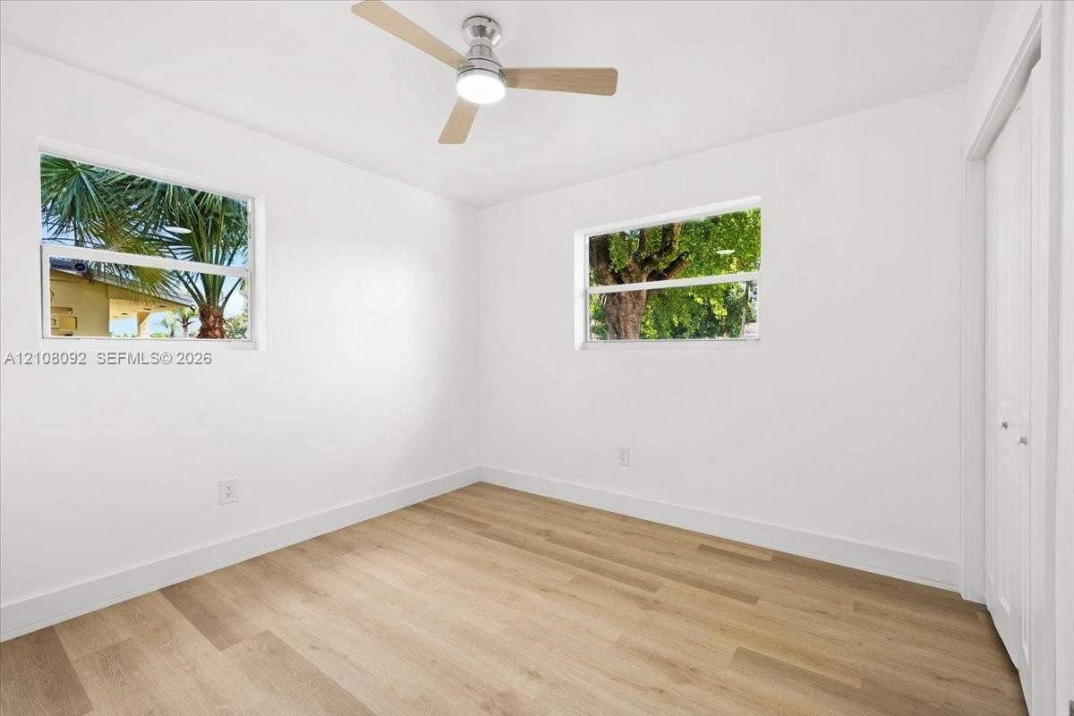 Interior space featuring wood-finish flooring, two dual-pane windows, a ceiling fan with integrated lighting, and a closet with bifold doors