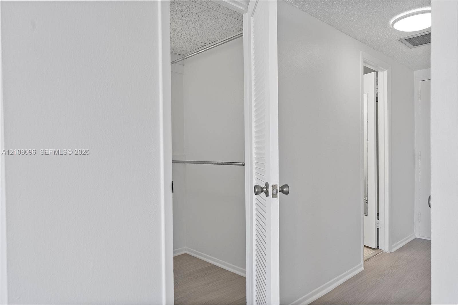 1965 S Ocean Drive, #6H, Hallandale Beach, Hallandale Beach, FL 33009 Walk-in closet featuring light-toned wood-finish flooring, white walls, and a metal hanging rod, complemented by a white louvered door with a brushed metallic knob