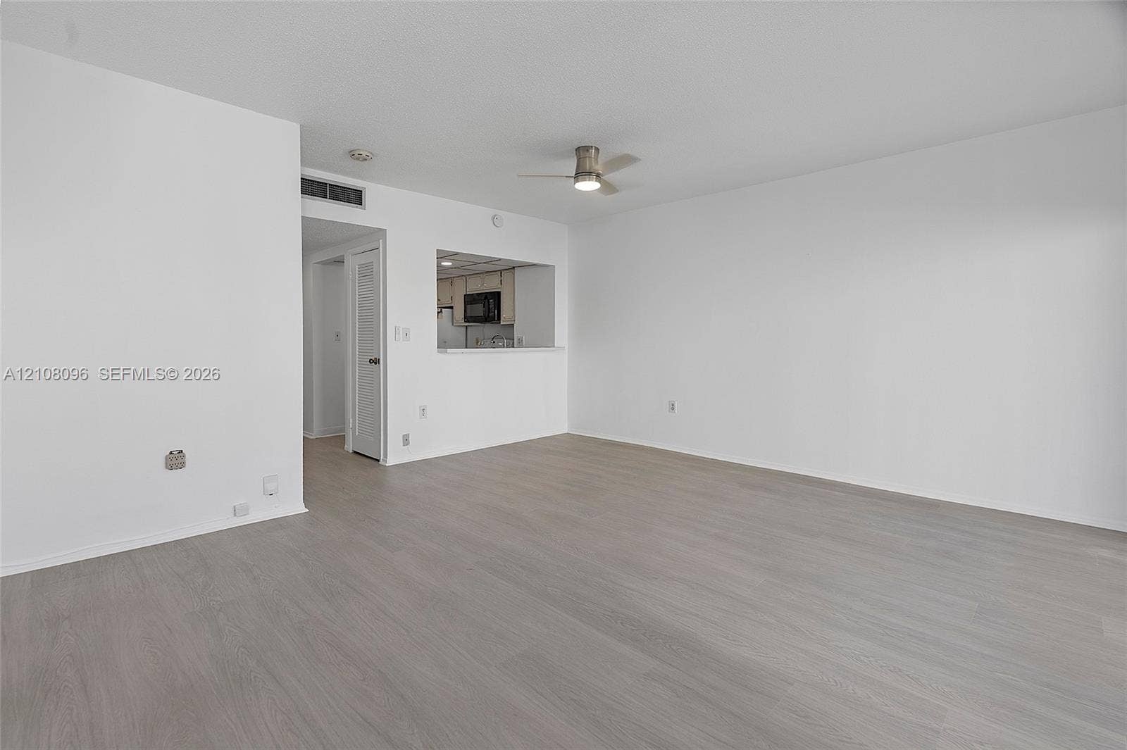 1965 S Ocean Drive, #6H, Hallandale Beach, Hallandale Beach, FL 33009 Open-concept interior featuring neutral wall tones, wood-finish flooring, a ceiling fan with integrated lighting, and a kitchen pass-through window