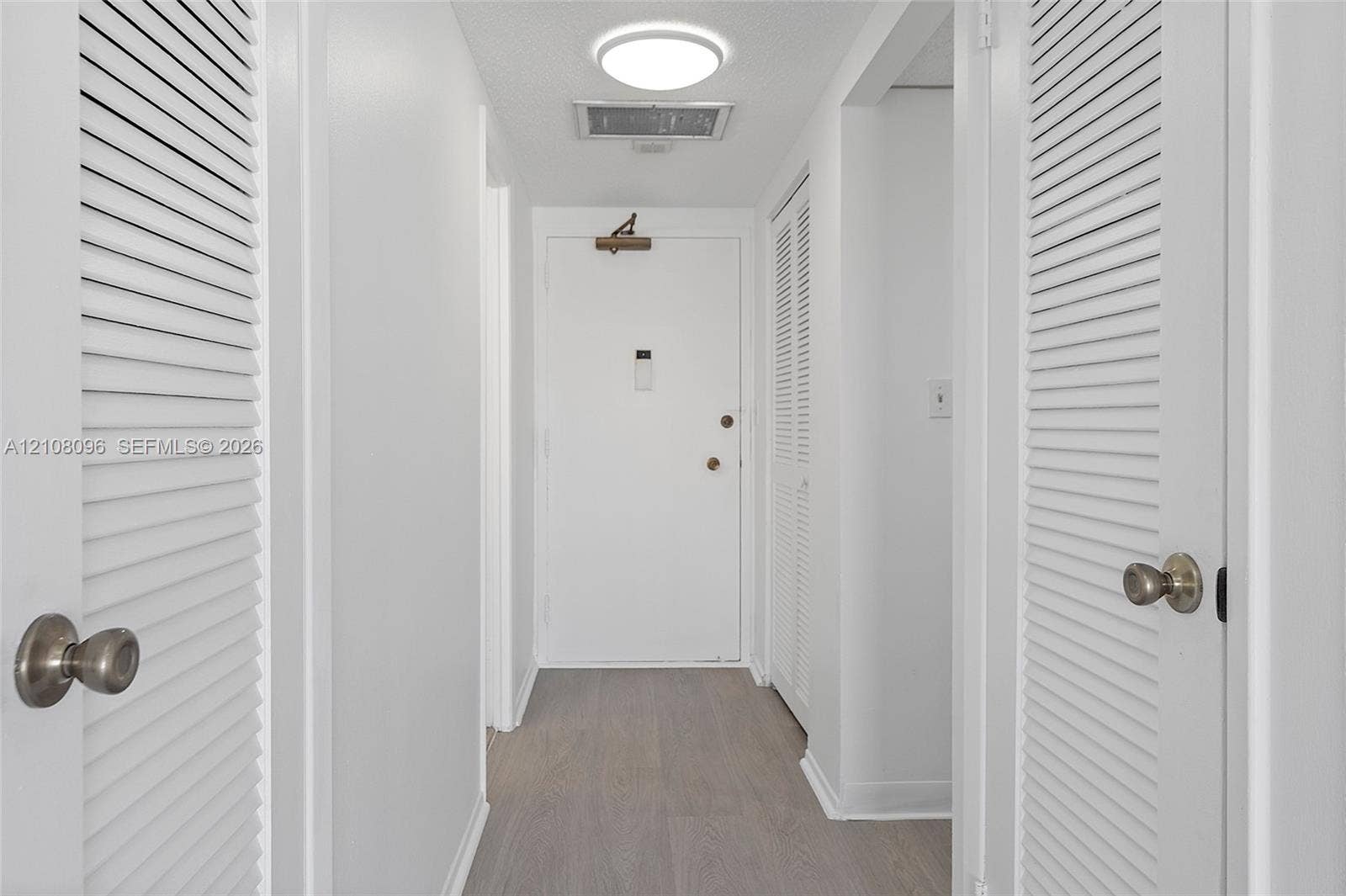 1965 S Ocean Drive, #6H, Hallandale Beach, Hallandale Beach, FL 33009 Interior hallway featuring wood-finish flooring, dual louvered closet doors with metallic hardware, and flush-mount ceiling lighting