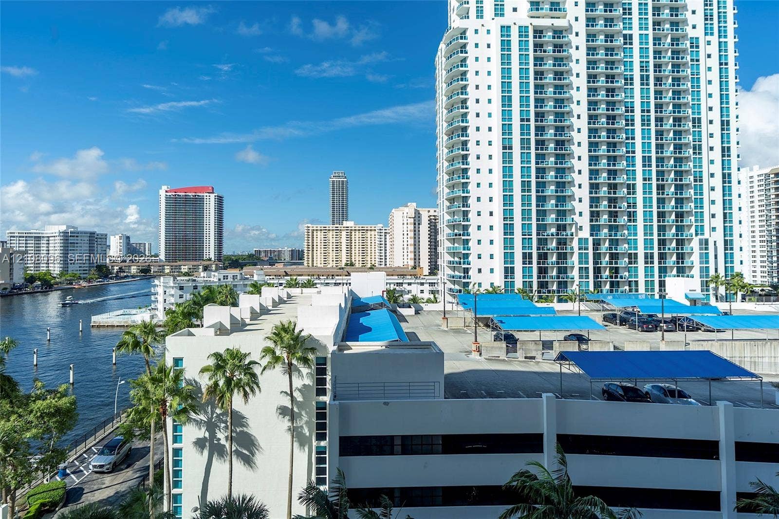 1965 S Ocean Drive, #6H, Hallandale Beach, Hallandale Beach, FL 33009 High-rise residential exterior with multi-level parking structure, blue canvas shade coverings, palm-lined perimeter, and waterfront access