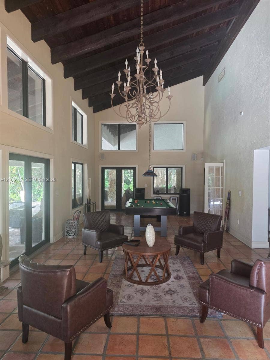High vaulted ceilings with exposed dark wood beams, terracotta tile flooring, multi-light chandelier, and expansive windows
