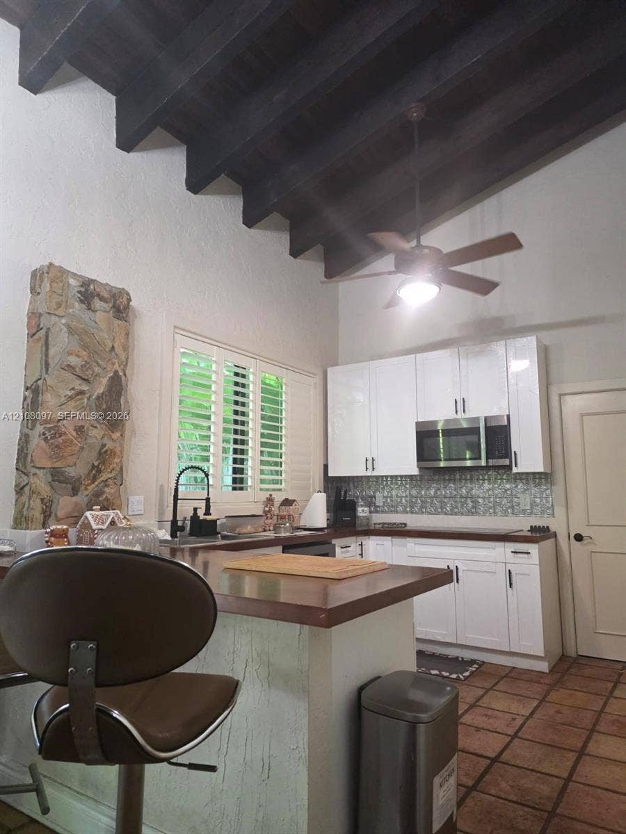 Kitchen featuring vaulted ceilings with exposed wood beams, stone accent wall, white cabinetry, tile flooring, and integrated countertop breakfast bar