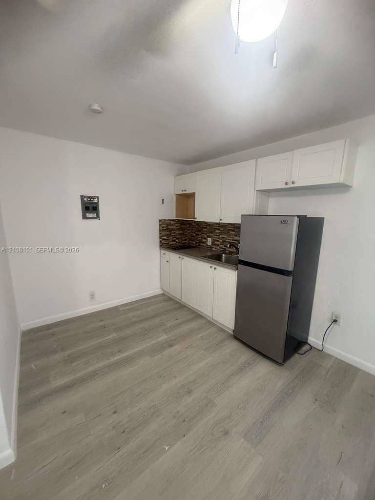 6318 Buchanan Street, #2, Hollywood, Hollywood, FL 33024 Kitchen featuring wood-finish flooring, white cabinetry, a multi-tonal decorative tile backsplash, and a stainless steel refrigerator