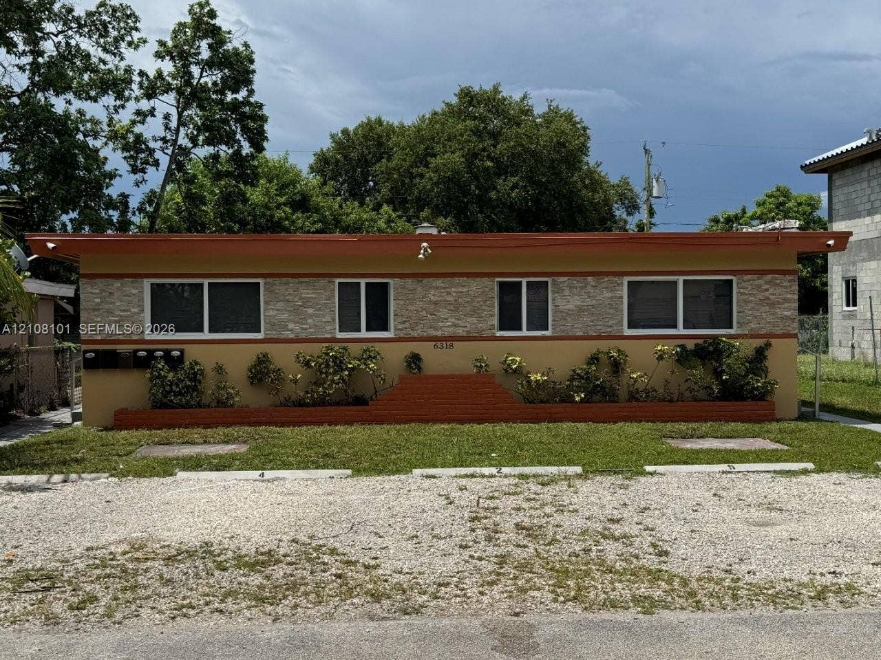 6318 Buchanan Street, #2, Hollywood, Hollywood, FL 33024 Single-story exterior featuring a stone-veneer facade, flat roofline, integrated brick planters, and designated gravel parking spaces