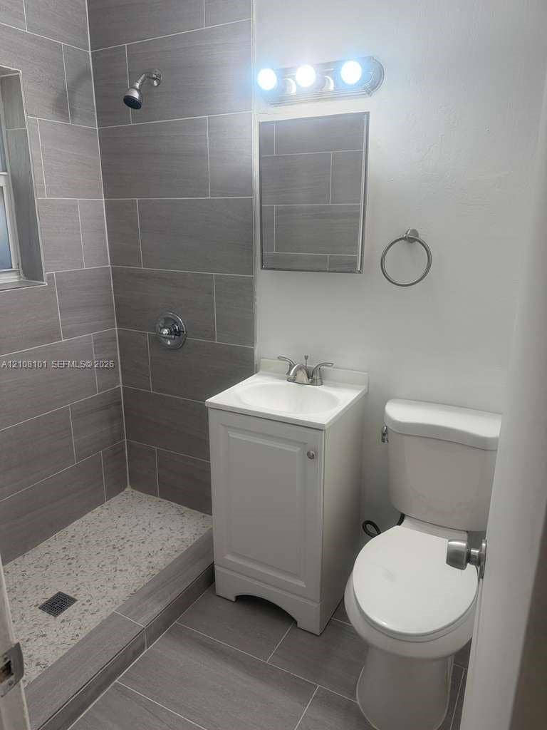 6318 Buchanan Street, #2, Hollywood, Hollywood, FL 33024 Bathroom featuring walk-in shower with large-format tile surround, integrated pebble-textured floor, white vanity cabinet with a ceramic sink, and vanity light fixture