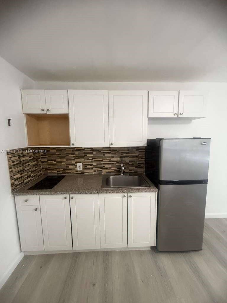 6318 Buchanan Street, #2, Hollywood, Hollywood, FL 33024 Kitchenette featuring white Shaker-style cabinetry, stone-texture countertops, mosaic tile backsplash, stainless steel sink, and wood-finish flooring