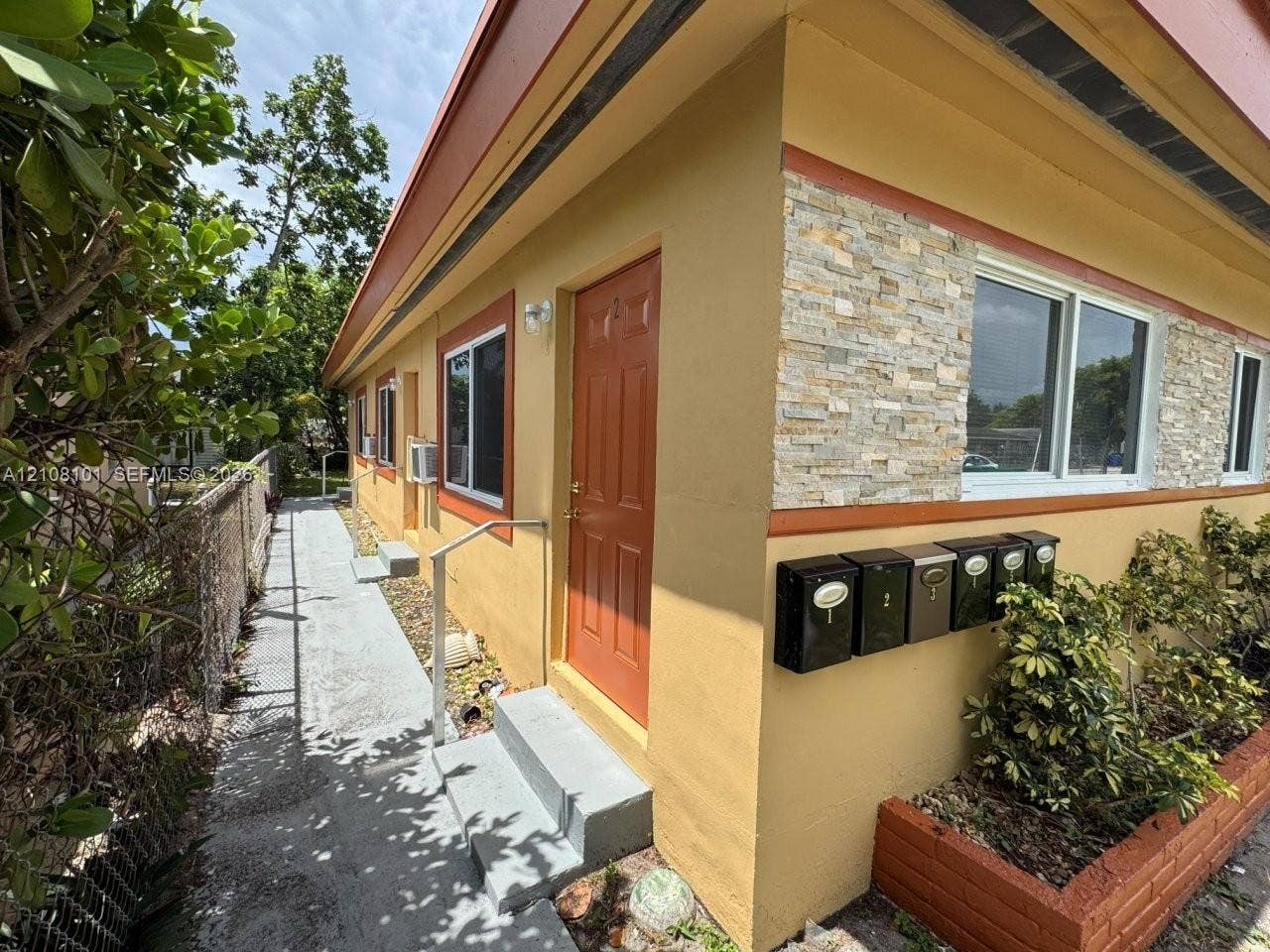 6318 Buchanan Street, #2, Hollywood, Hollywood, FL 33024 Exterior featuring a stucco facade with stacked stone veneer accents, multi-unit wall-mounted mailboxes, concrete steps with metal handrails, and a brick-lined landscape bed