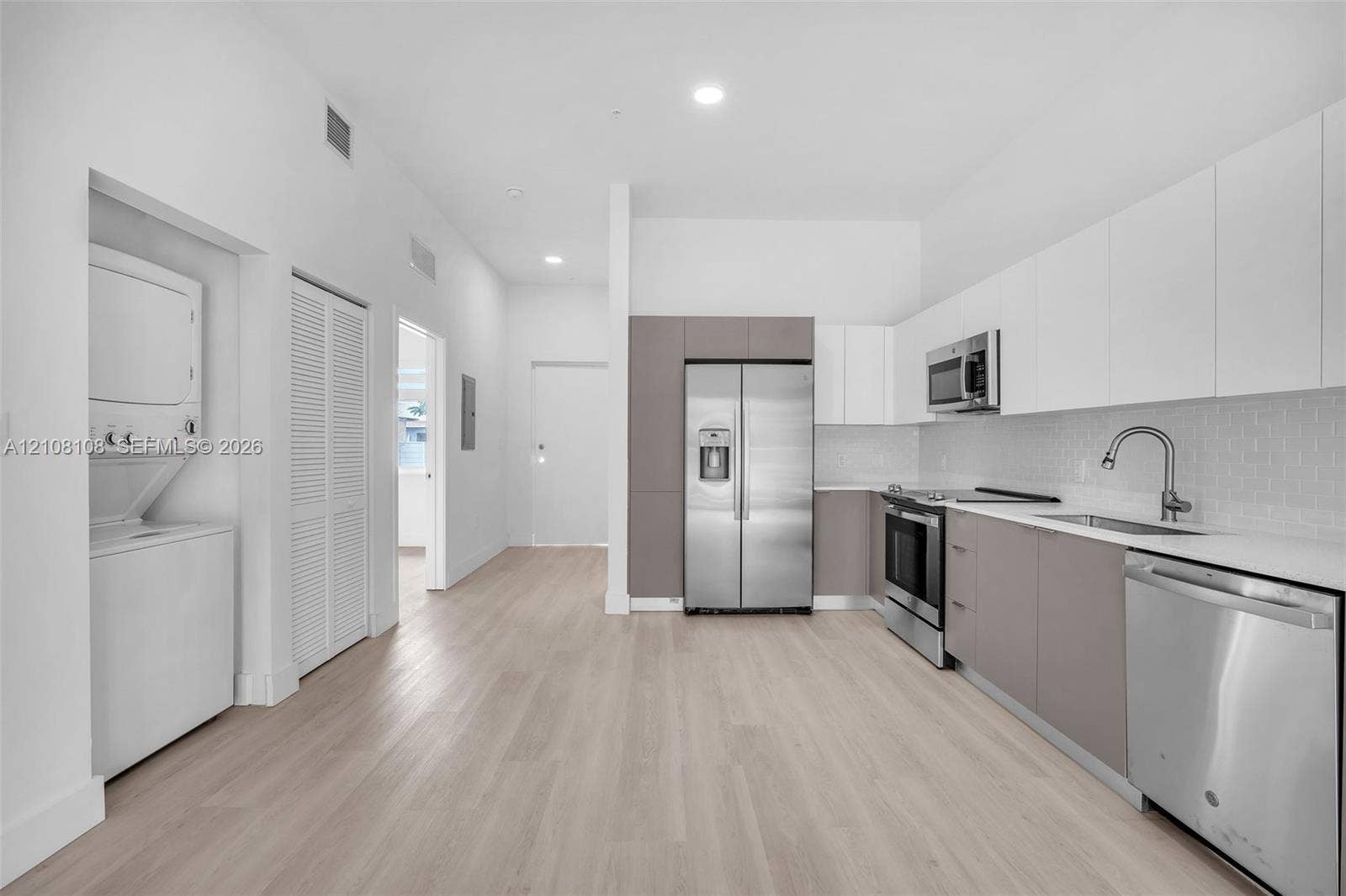 605 N Dixie Highway, #B207, Hallandale Beach, Hallandale Beach, FL 33009 Kitchen featuring white and grey flat-panel cabinetry, stainless steel appliances, subway tile backsplash, and light-toned wood-finish flooring with an integrated laundry area