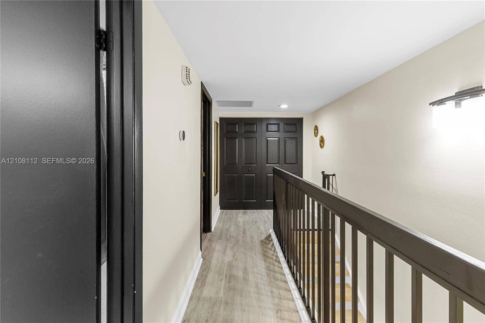 1431 NW 112th Terrace, Pembroke Pines, FL 33026 Hallway featuring wood-finish flooring, dark-toned interior doors, and a matching handrail with vertical balusters
