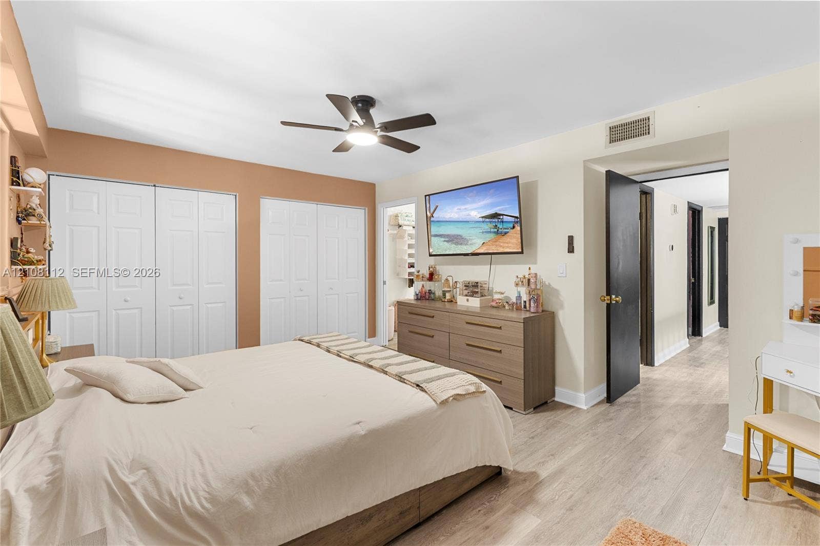 1431 NW 112th Terrace, Pembroke Pines, FL 33026 Neutral-tone interior space featuring wood-finish flooring, dual sets of bi-fold closet doors, and a ceiling fan with integrated lighting