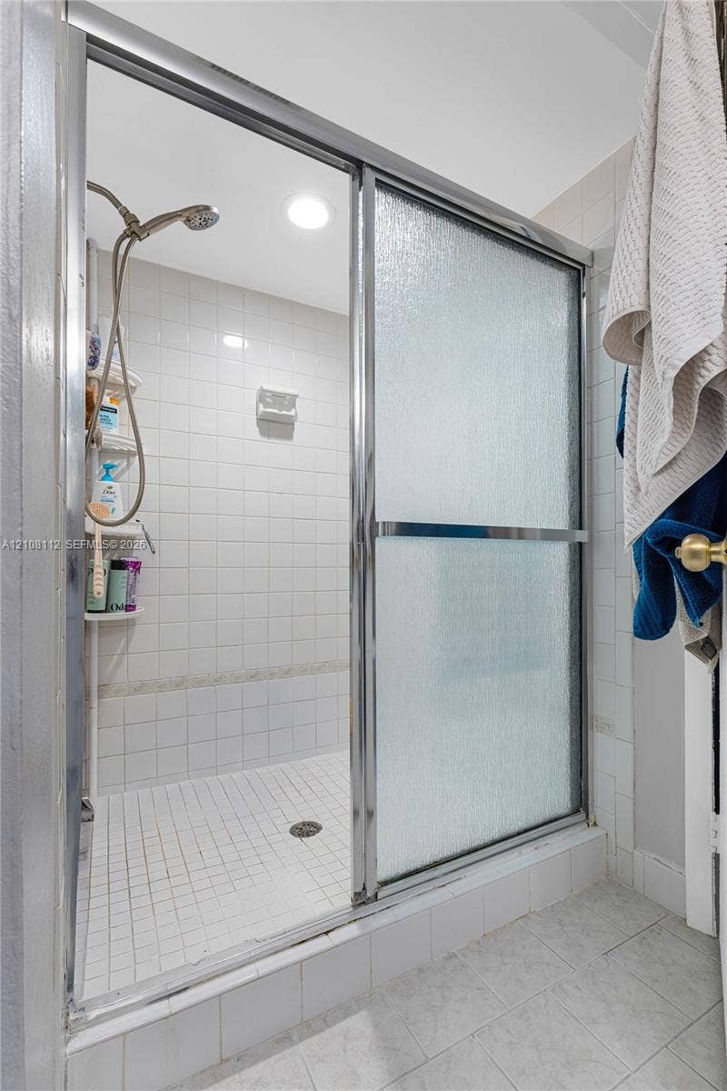 1431 NW 112th Terrace, Pembroke Pines, FL 33026 Shower enclosure featuring a chrome-framed sliding glass door, white tiled walls, a handheld shower fixture, and a built-in corner shelving unit