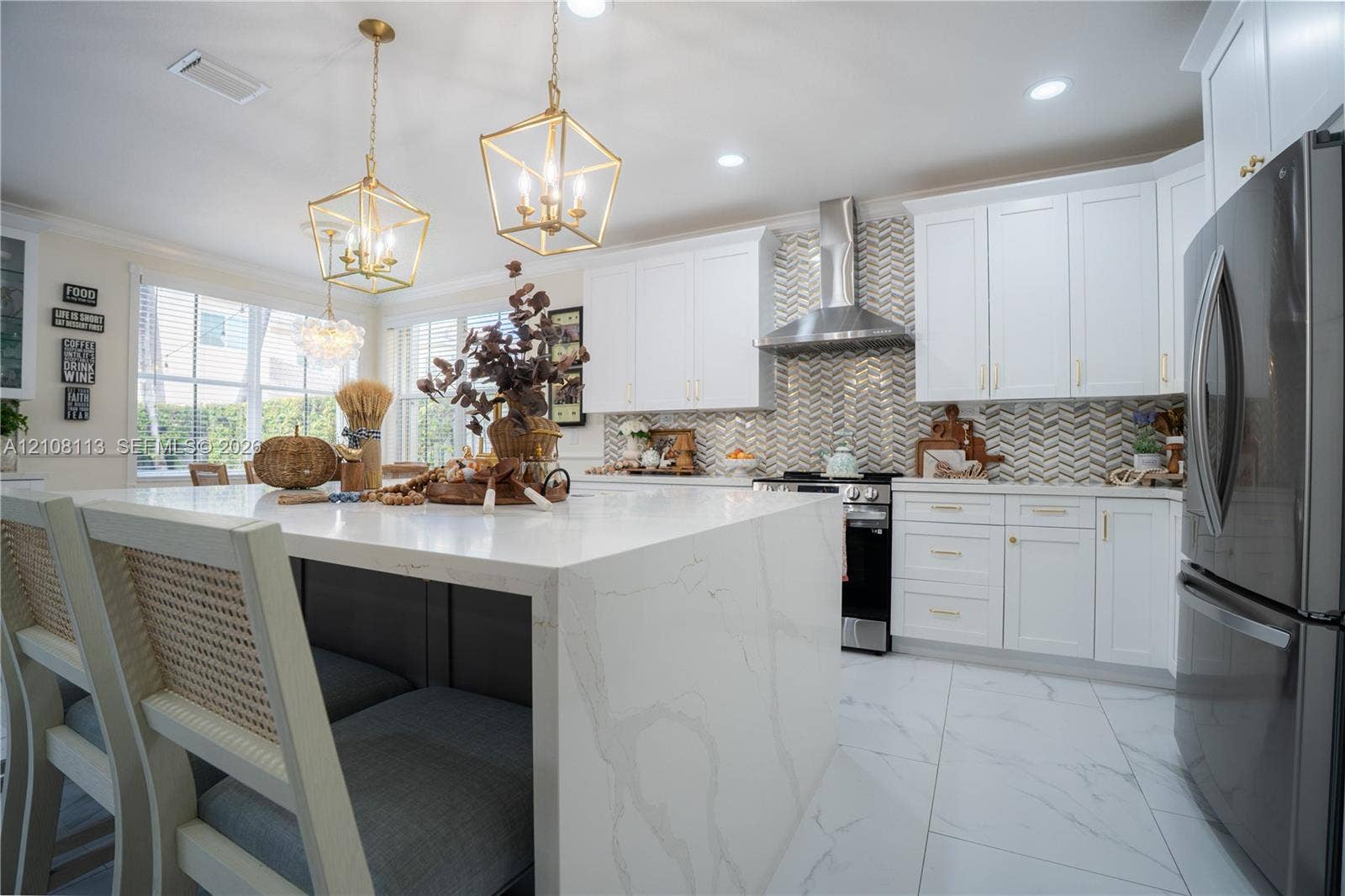 2294 SW 126th Avenue, Miramar, FL 33027 Kitchen featuring a waterfall-edge stone island, white shaker-style cabinetry, herringbone-patterned tile backsplash, stainless steel chimney-style range hood, and large-format tile flooring