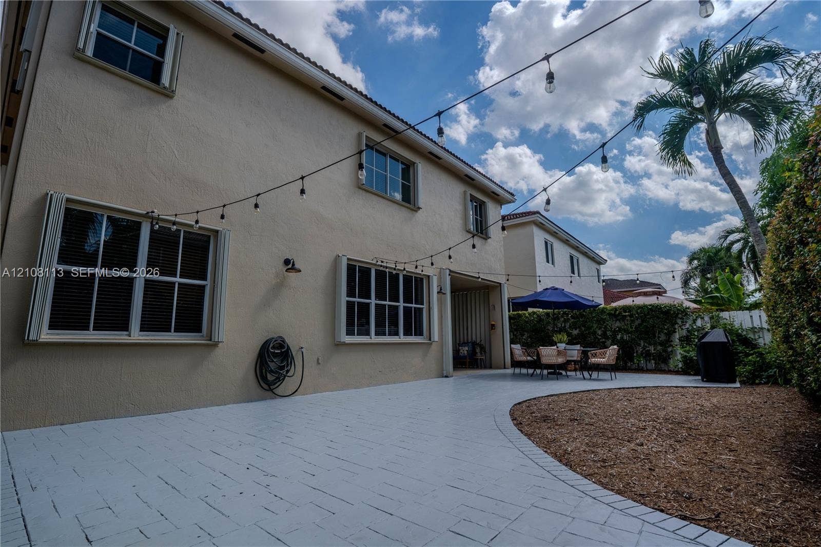 2294 SW 126th Avenue, Miramar, FL 33027 Expansive paved patio featuring integrated string lighting, stucco exterior cladding, multi-pane windows, and manicured landscaping