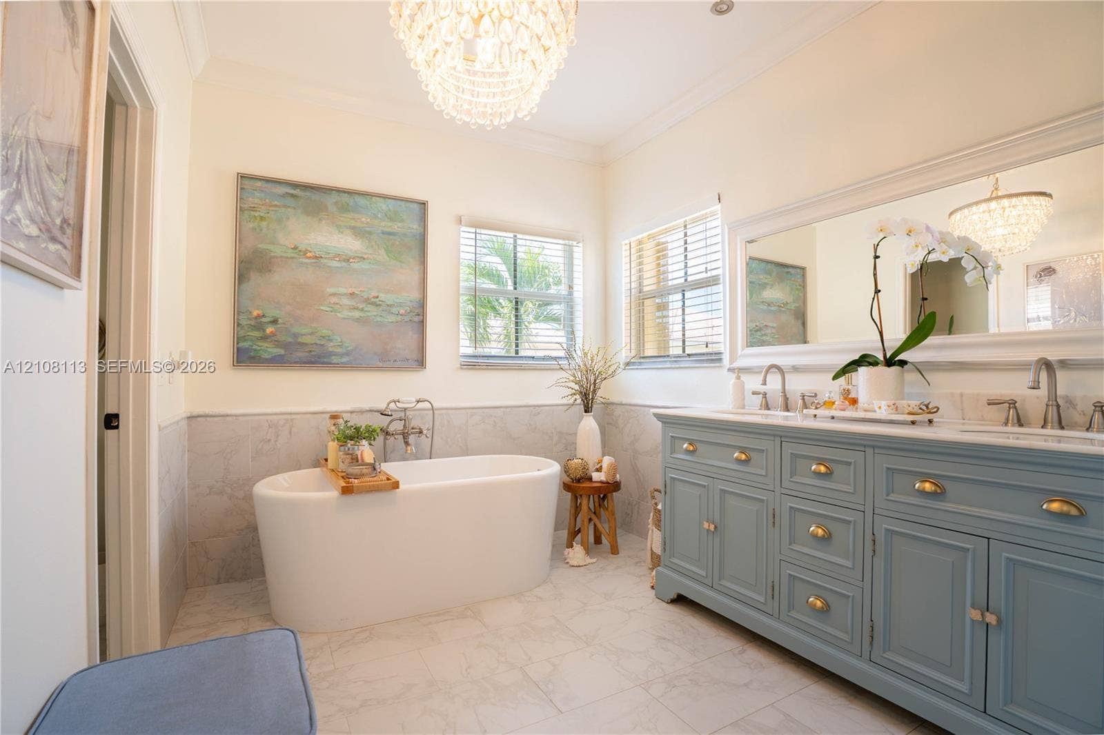 2294 SW 126th Avenue, Miramar, FL 33027 Freestanding soaking tub with wall-mounted plumbing, dual-sink vanity with brass-finish hardware, stone-finish flooring, half-wall tile wainscoting, and tiered crystal chandelier lighting