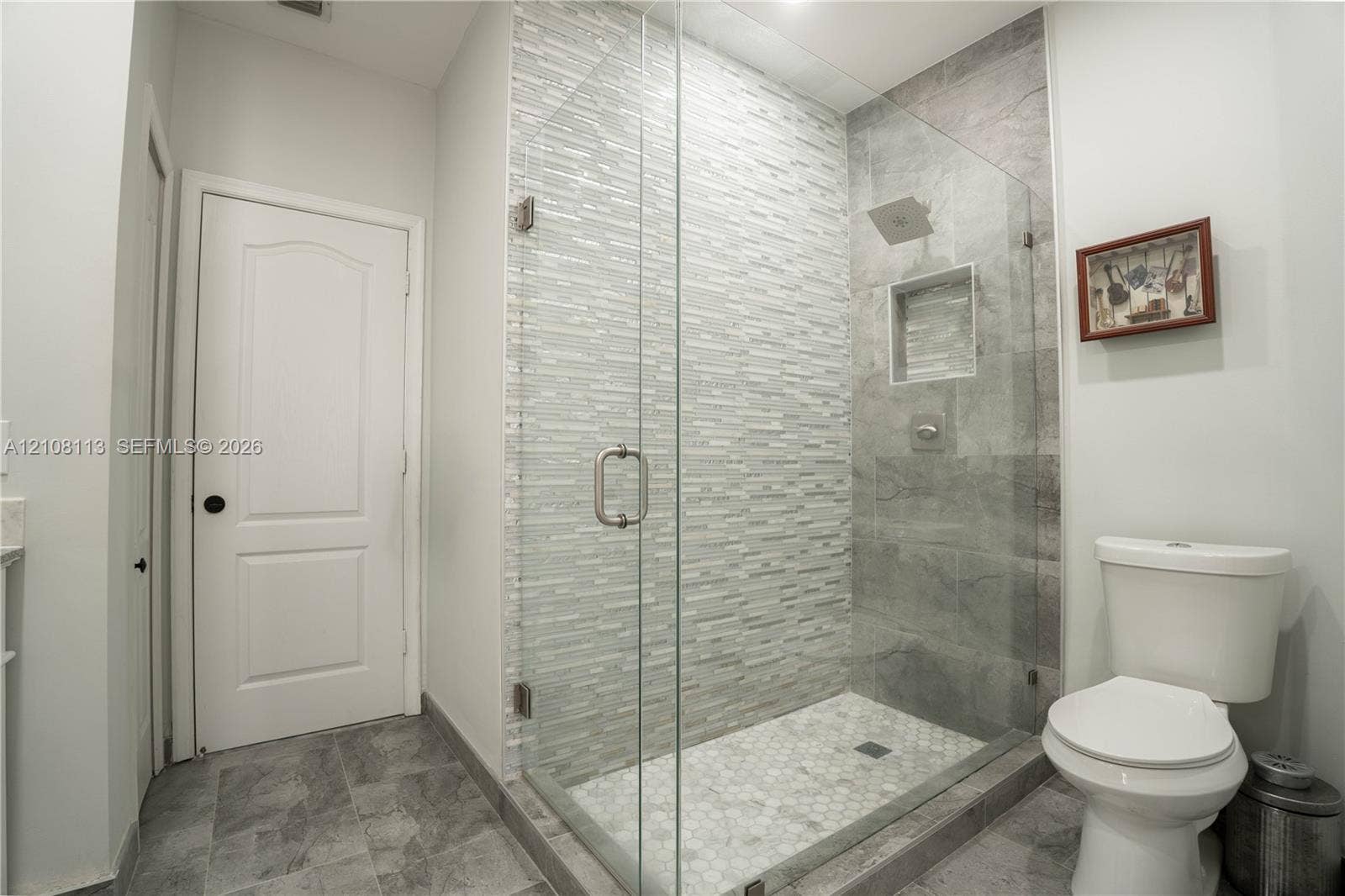 2294 SW 126th Avenue, Miramar, FL 33027 Walk-in shower featuring a frameless glass enclosure, stacked stone accent wall, inset wall niche, and hexagon tile floor