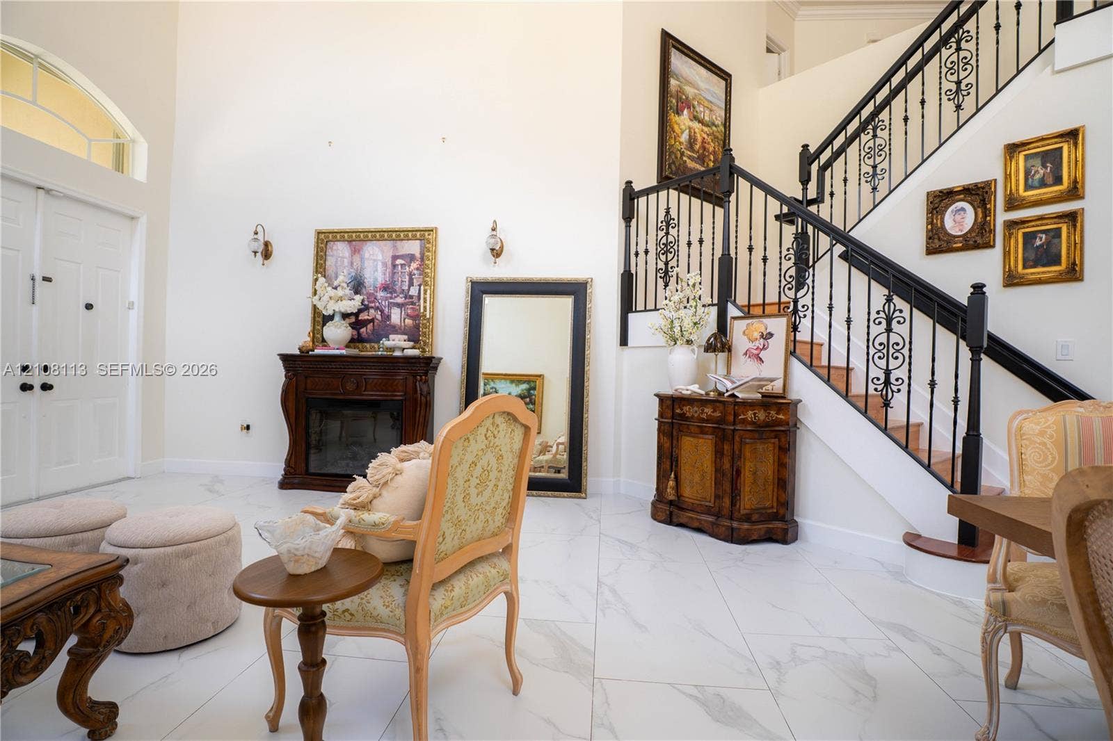 2294 SW 126th Avenue, Miramar, FL 33027 Grand entry featuring double front doors, vaulted ceilings, light-toned stone-finish tile flooring, a staircase with decorative wrought-iron railings, and an integrated dark wood-finish fireplace