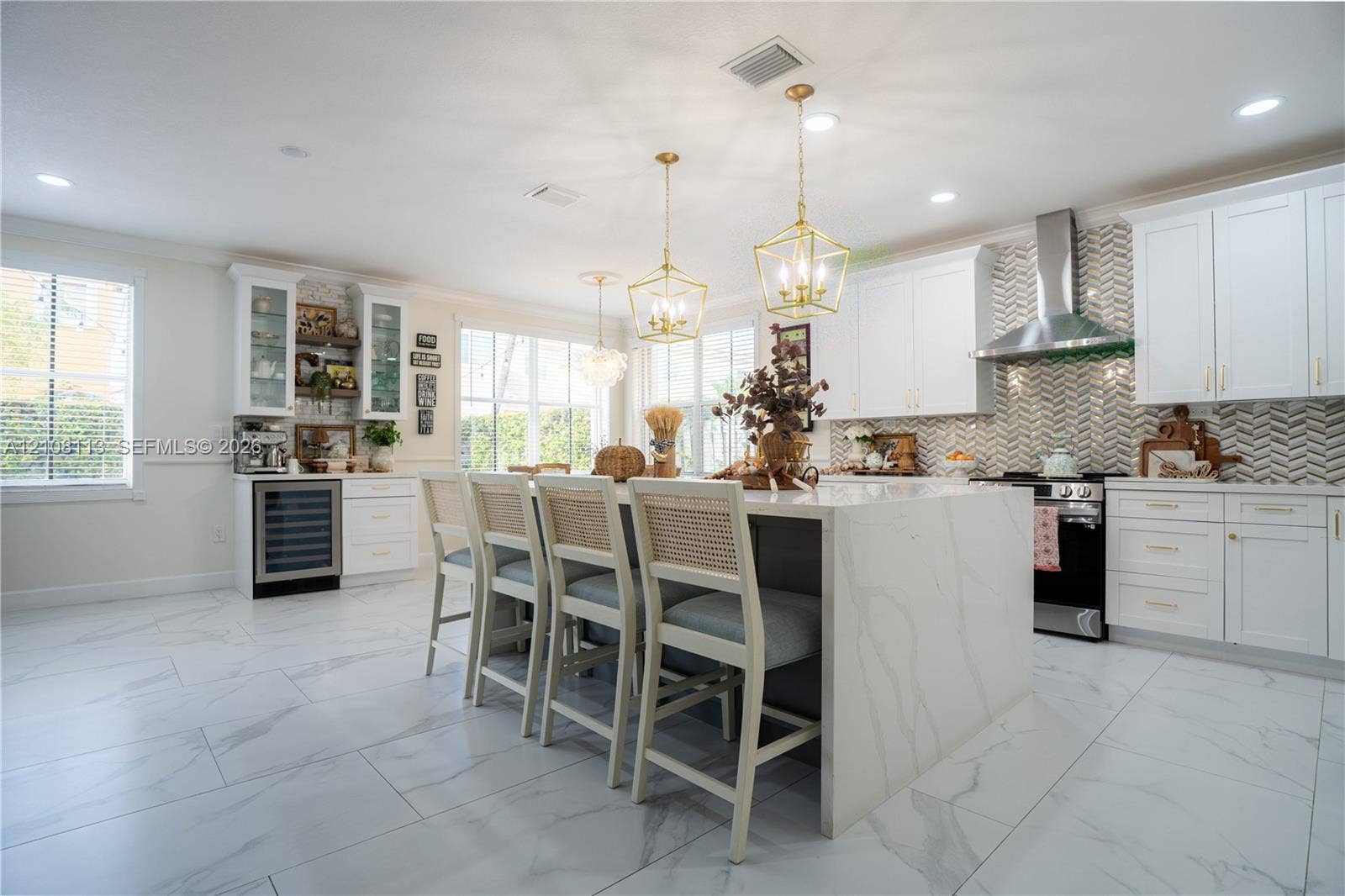 2294 SW 126th Avenue, Miramar, FL 33027 Kitchen featuring a central island with stone-finish waterfall edges, herringbone-patterned tile backsplash, white shaker-style cabinetry, stainless steel range hood, and porcelain tile flooring
