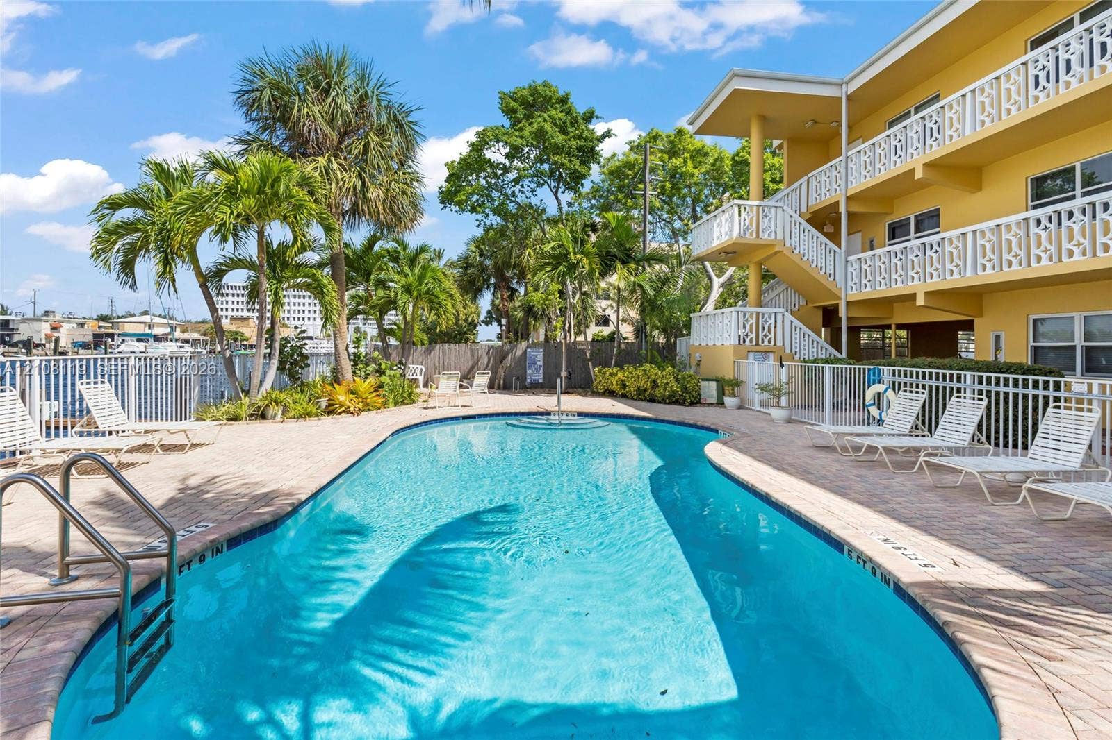 Swimming pool featuring a paver stone deck, palm tree landscaping, and metal perimeter fencing