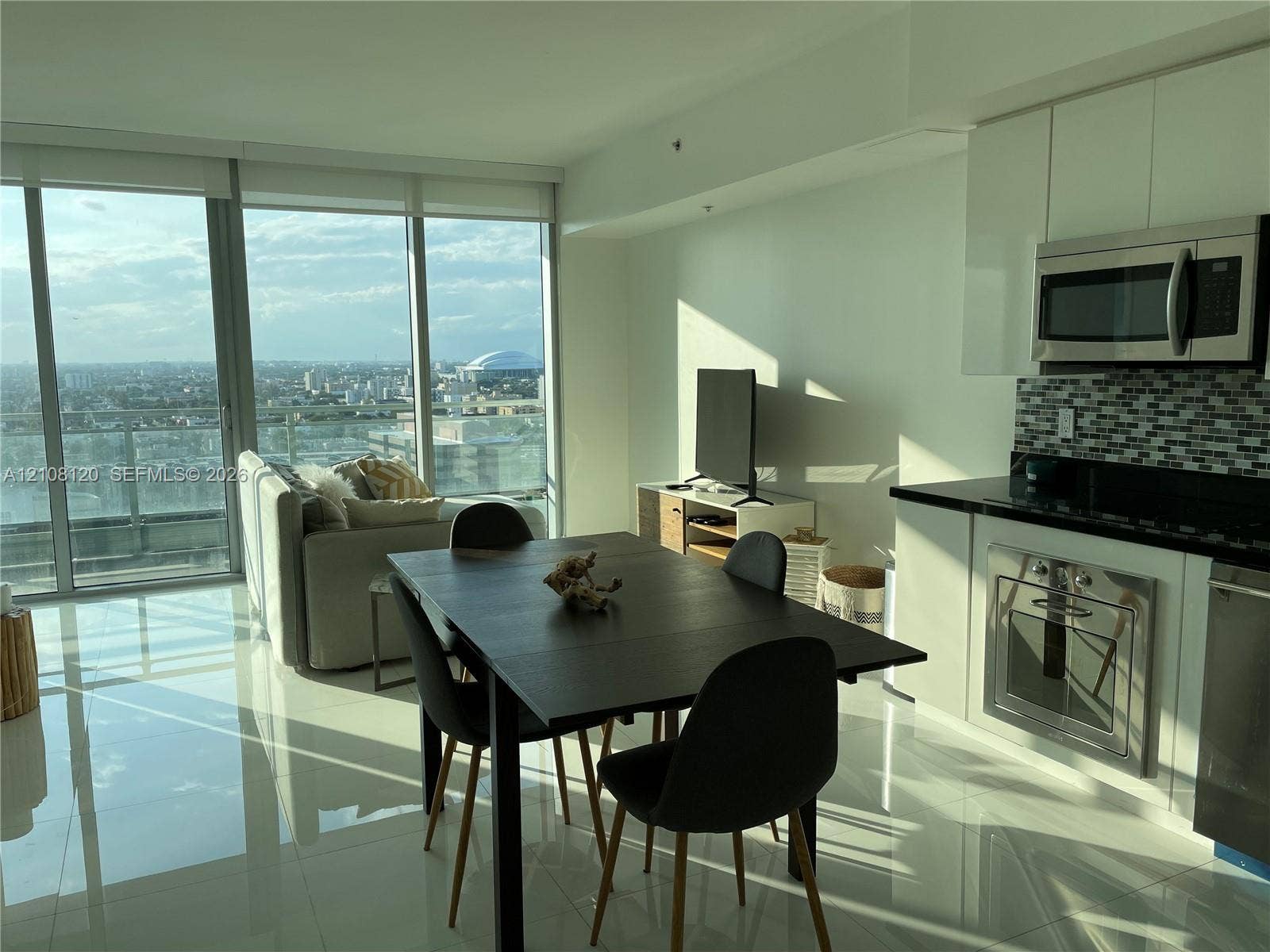 92 SW 3rd Street, #2307, Miami, FL 33130 Floor-to-ceiling windows, high-gloss white cabinetry, mosaic tile backsplash, stainless steel appliances, and polished tile flooring