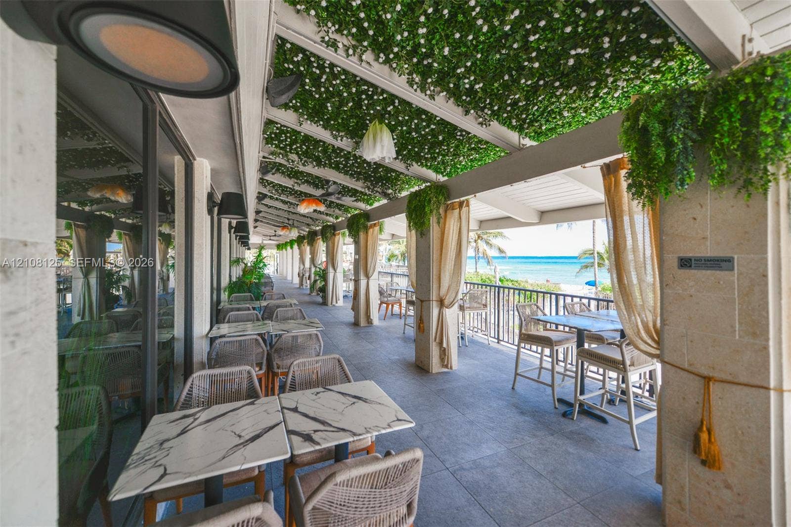 1985 S Ocean Drive, #8M, Hallandale Beach, FL 33009 Covered outdoor patio featuring stone tile flooring, a pergola roof with integrated greenery, natural stone support columns, and metal perimeter railing