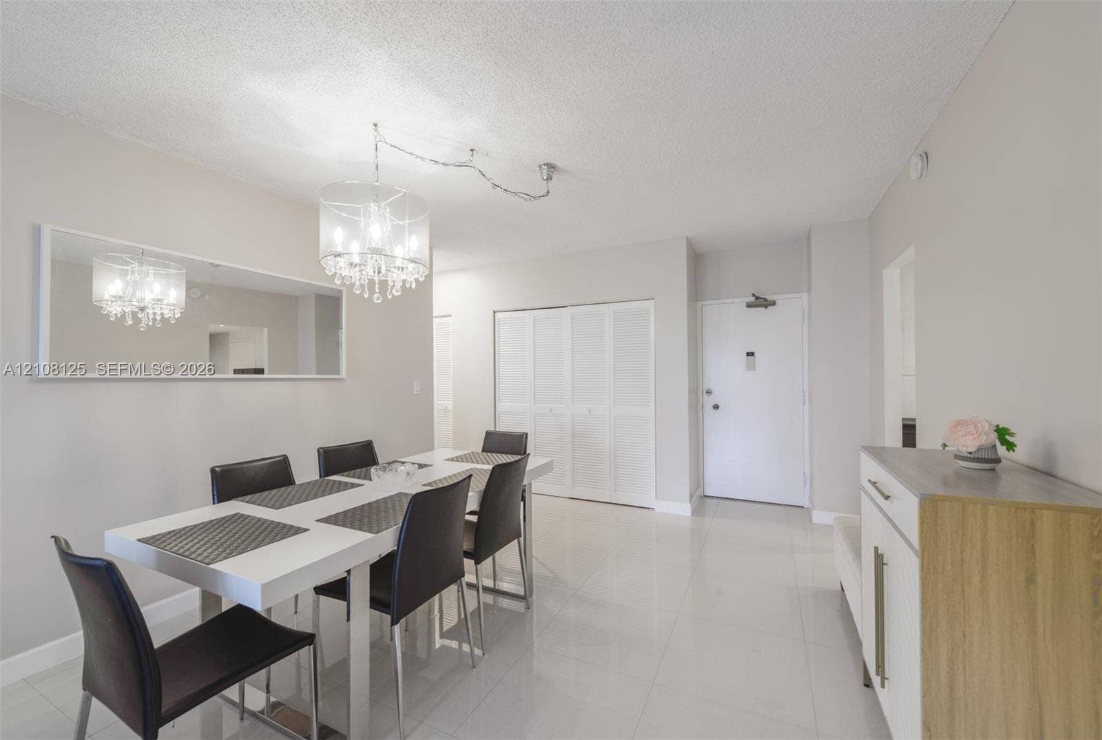 1985 S Ocean Drive, #8M, Hallandale Beach, FL 33009 Neutral-toned interior featuring polished tile flooring, a large wall-mounted mirror, a multifaceted crystal chandelier, and louvered double-door closets