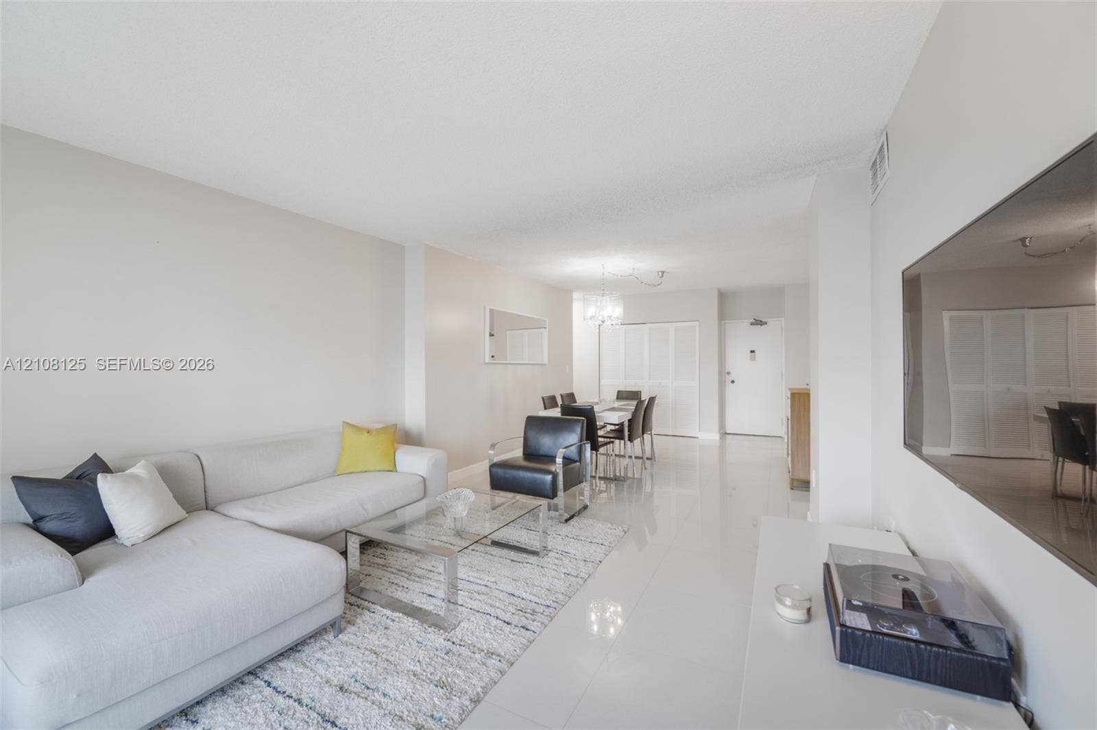 1985 S Ocean Drive, #8M, Hallandale Beach, FL 33009 Open-concept interior featuring light-toned tile flooring, neutral wall paint, a multi-light chandelier, and full-height bi-fold closet doors