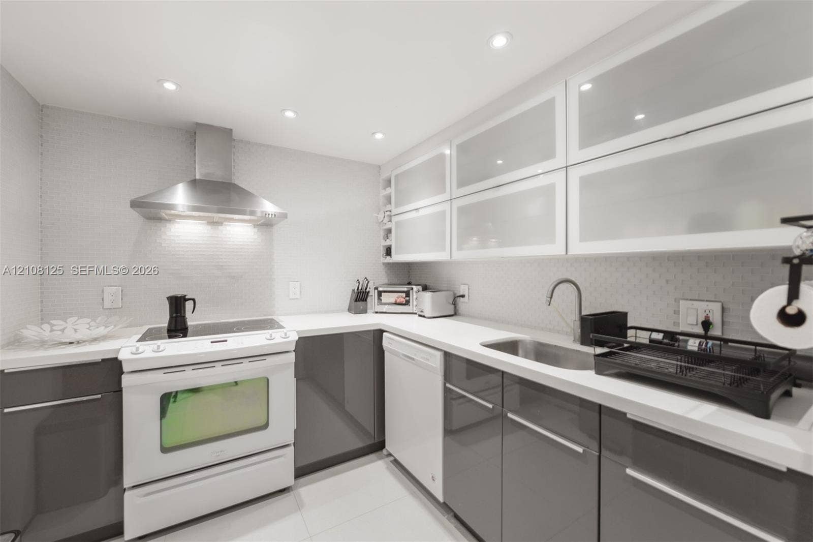 1985 S Ocean Drive, #8M, Hallandale Beach, FL 33009 Kitchen featuring high-gloss gray lower cabinetry, white upper cabinetry with frosted glass inserts, stone countertops, stainless steel range hood, and integrated recessed lighting