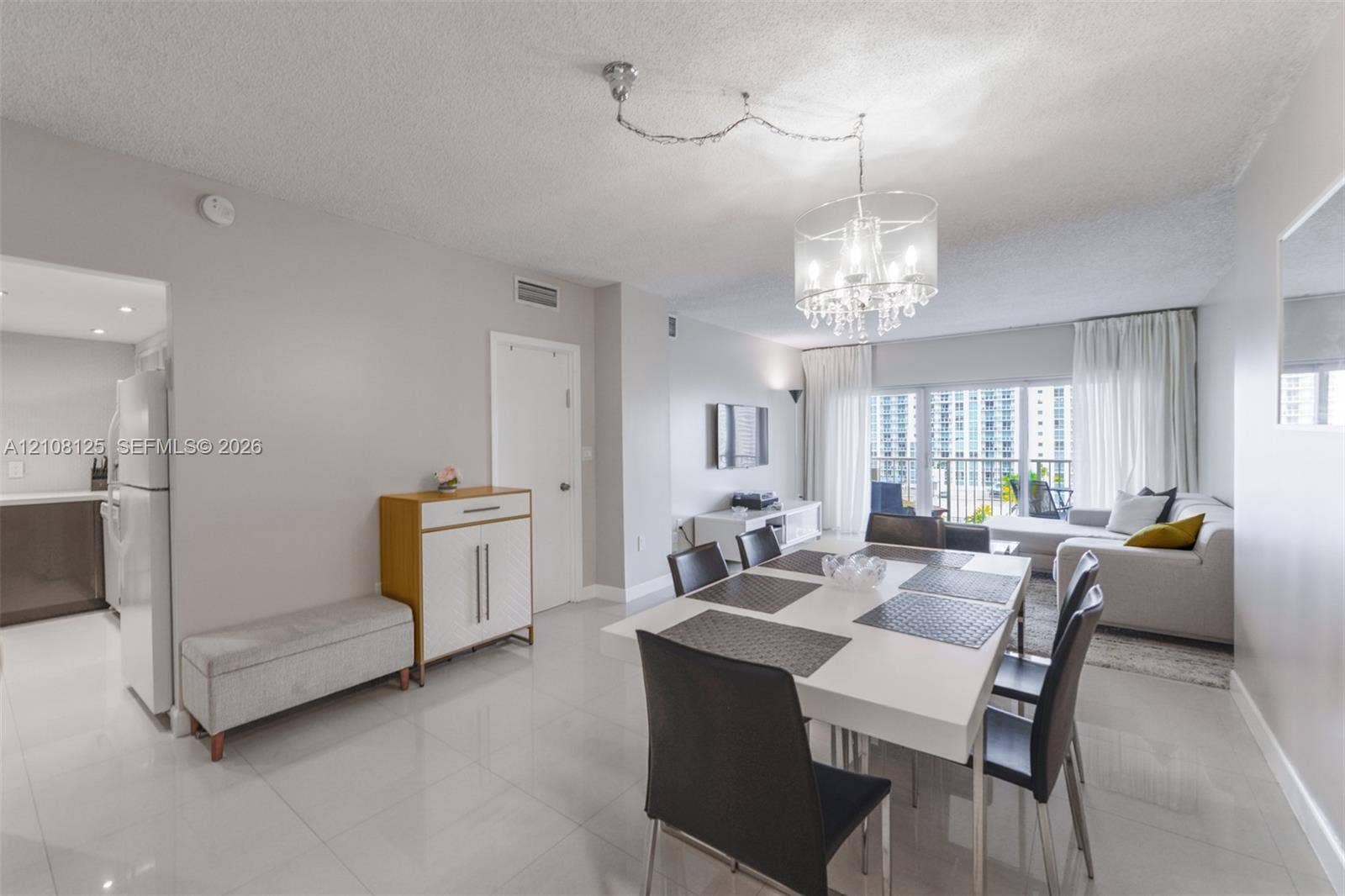1985 S Ocean Drive, #8M, Hallandale Beach, FL 33009 Open-concept living space featuring large-format tile flooring, a multi-light crystal chandelier, and floor-to-ceiling glass sliding doors providing natural light